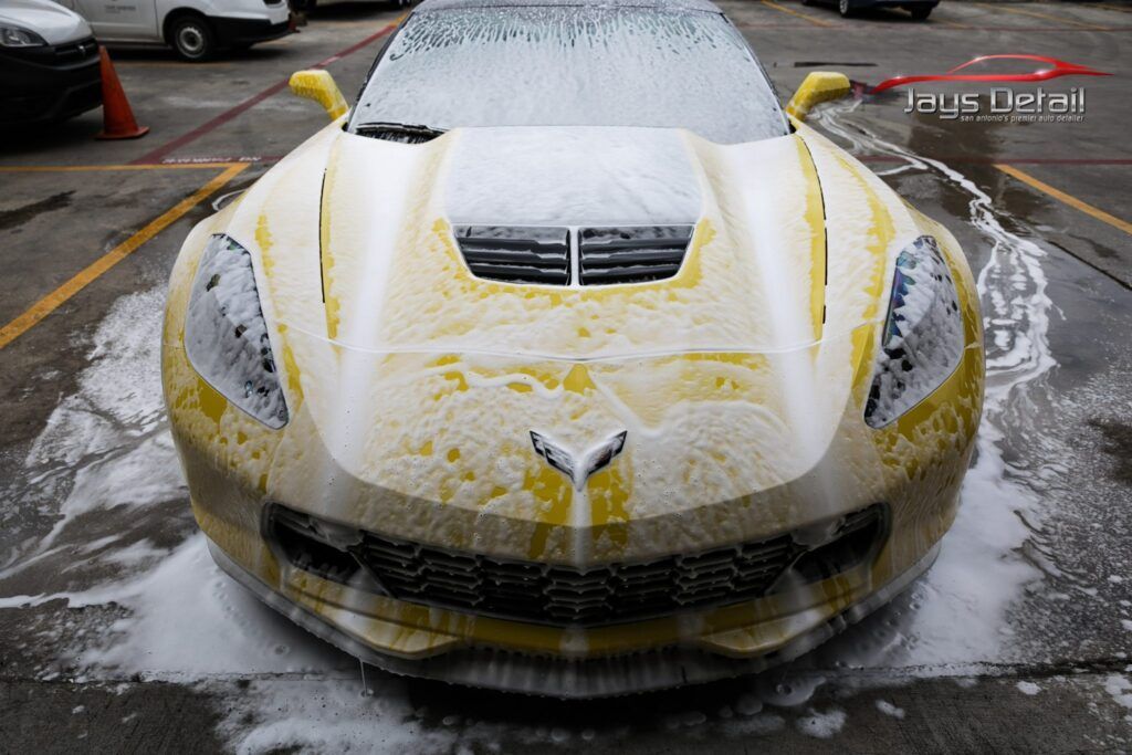 Yellow sports car covered in foamy soap, being washed at a car wash.