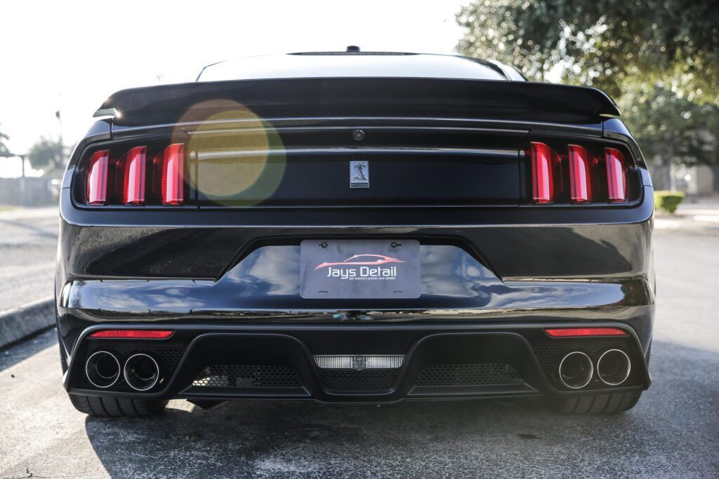 Black Ford Mustang rear view with red taillights, showing exhaust pipes and spoiler.