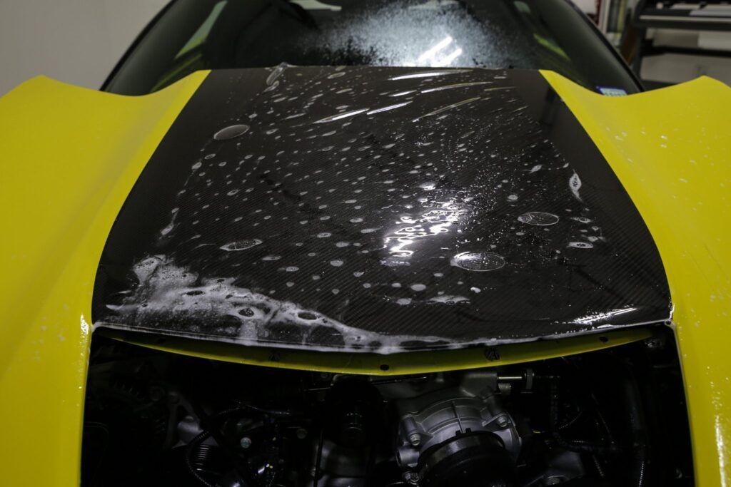 Yellow car hood with black racing stripe, covered in soapy water.