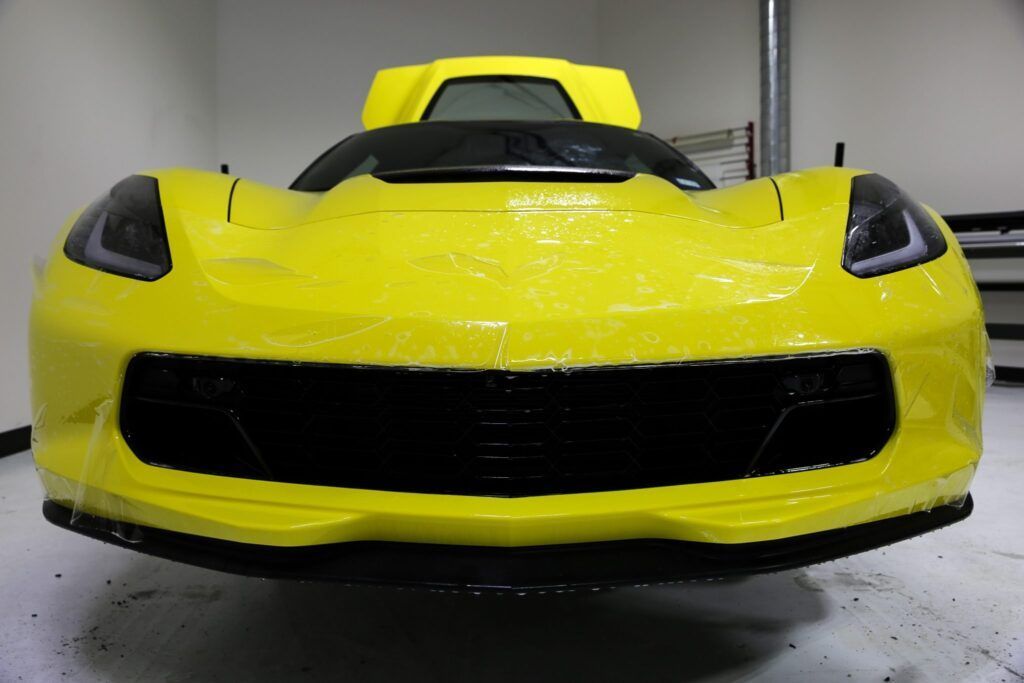 Yellow Corvette sports car in a workshop, covered in protective film.