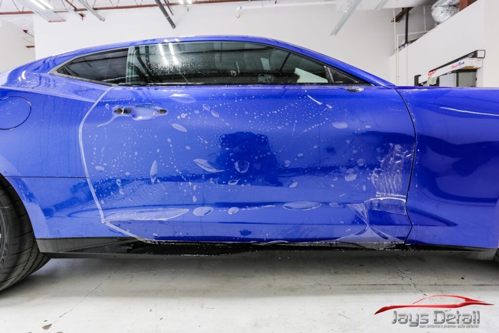 Blue car with protective film applied, in a detail shop.
