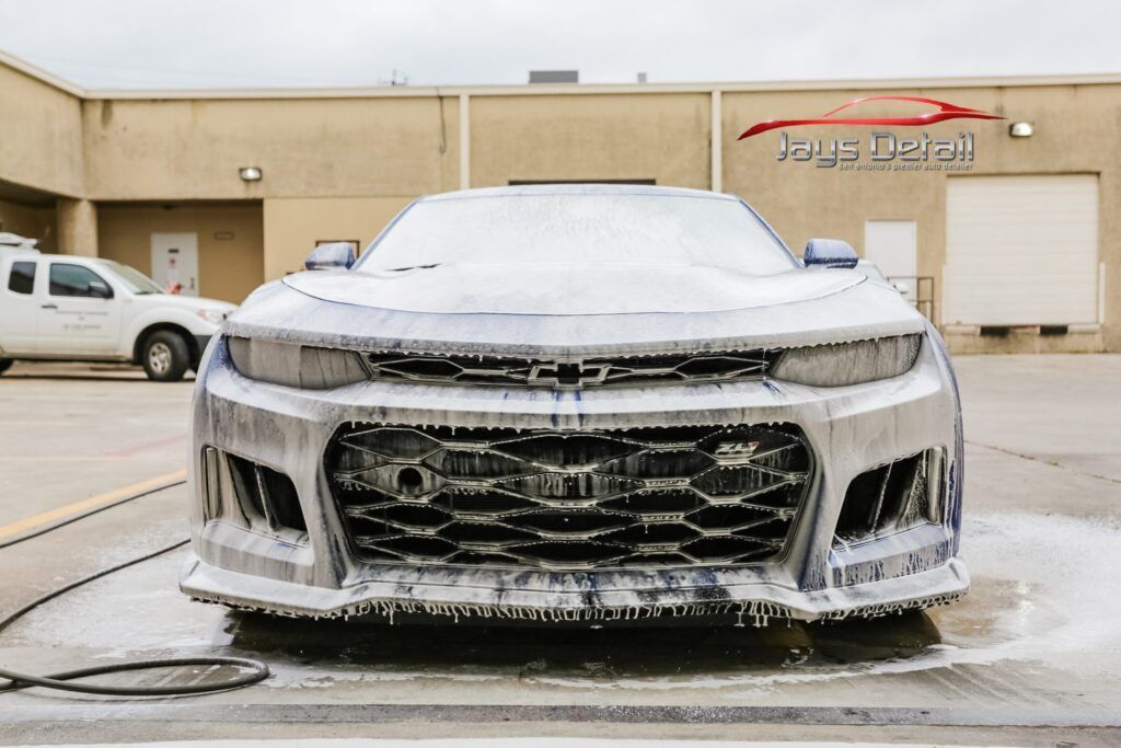 Ford Mustang covered in white foam at a car wash, viewed from the front.