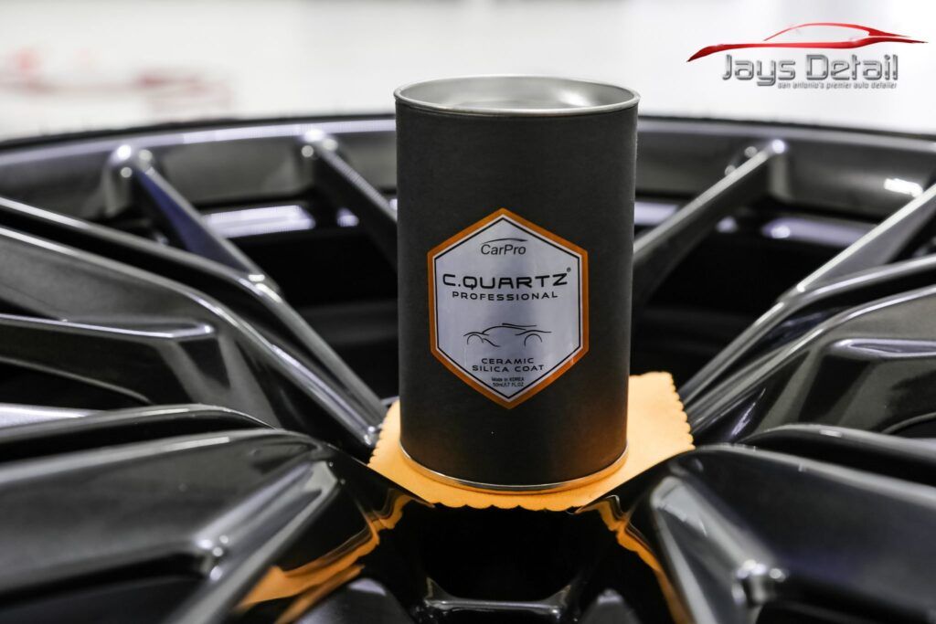 A black cylindrical container sits on an orange pad on a shiny black car rim.