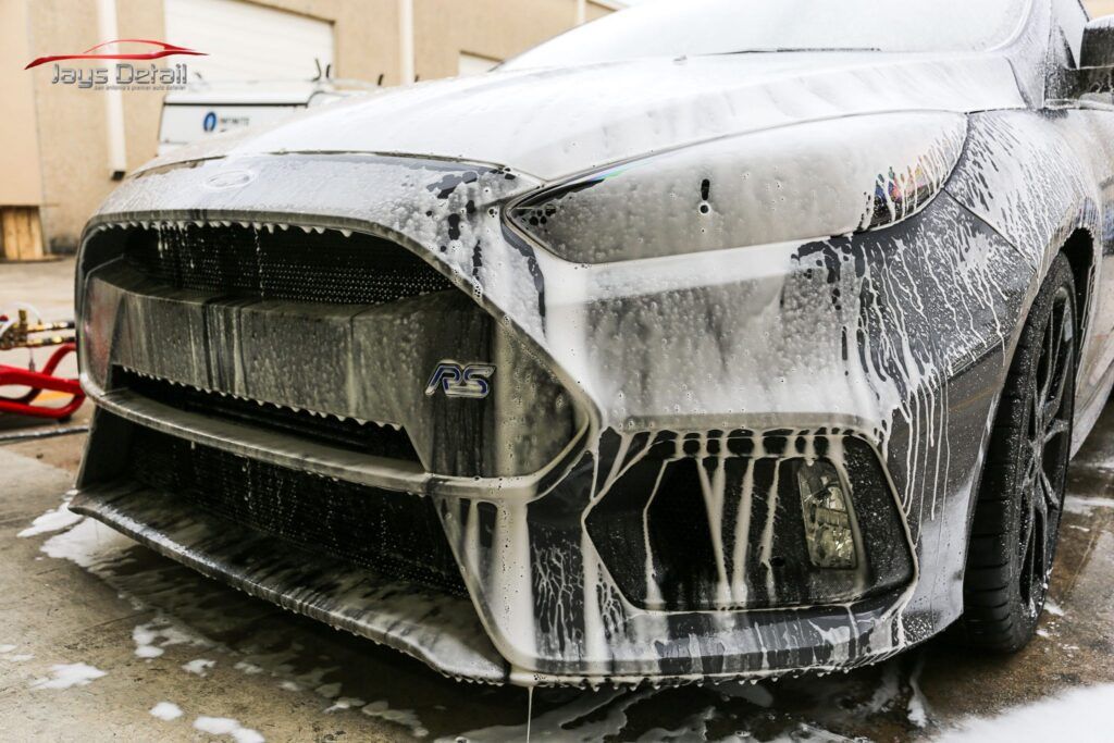 Black car covered in foamy soap suds, during a car wash.