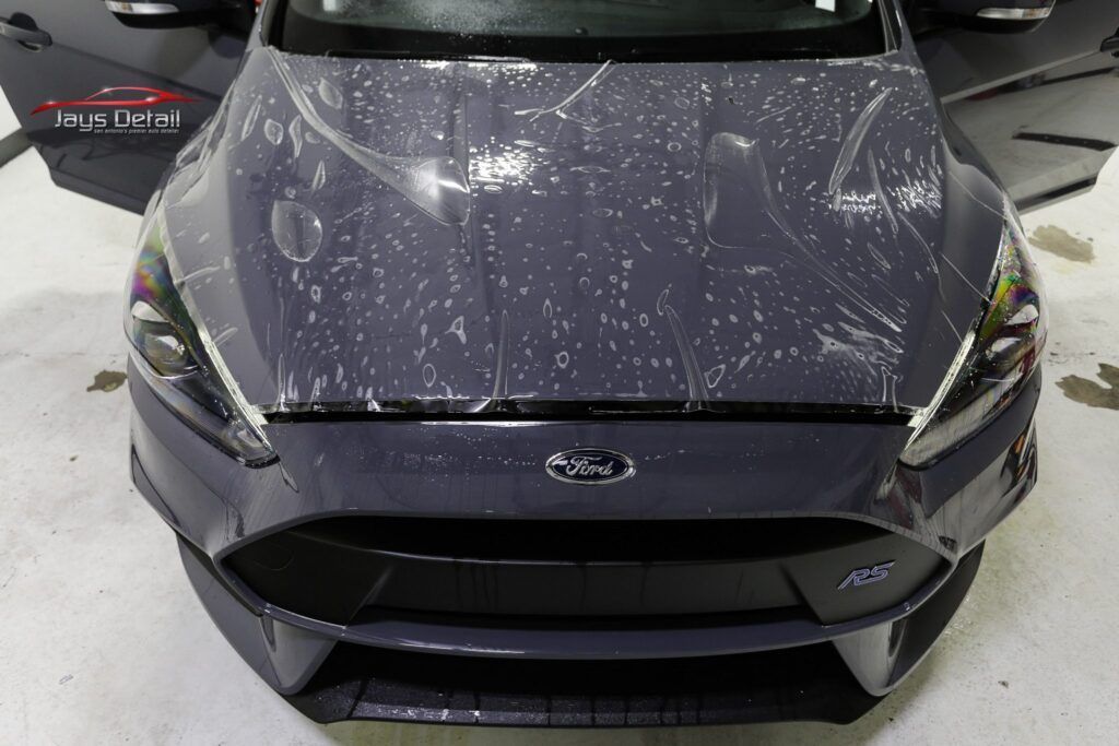 Dark gray Ford Focus with protective film on the hood, parked indoors.