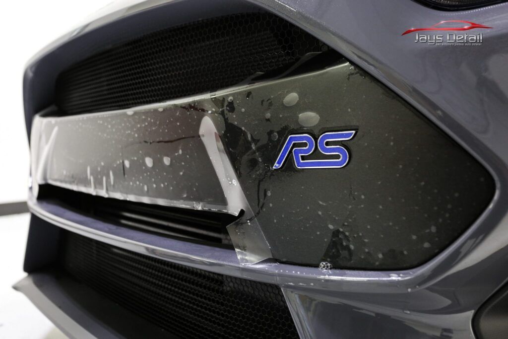 Close-up of a gray Ford Focus RS bumper with peeling paint protection film and the blue