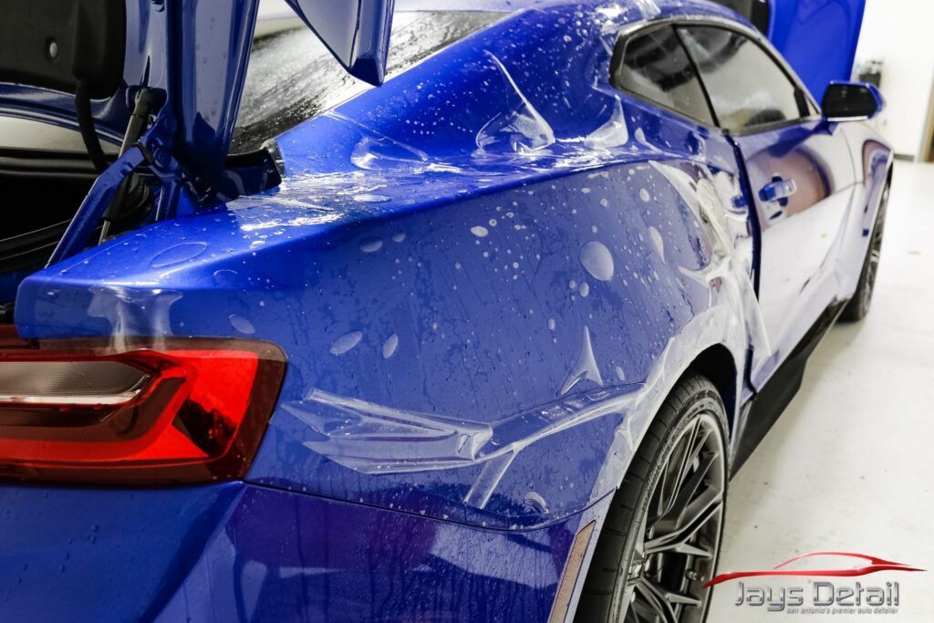 Blue car with clear film being applied; rear quarter panel, taillight detail.