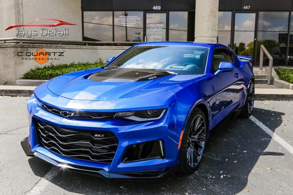 Blue Chevrolet Camaro in front of a business with a black hood.