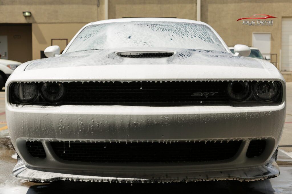 White Dodge Challenger covered in soapy foam at a car wash.