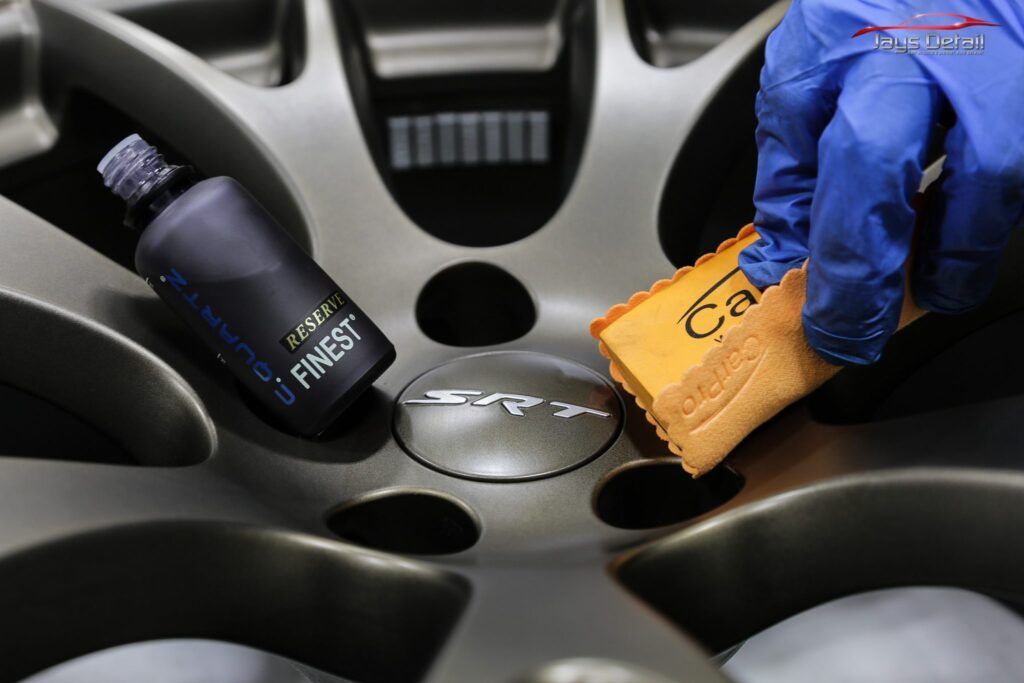 Person wearing blue glove applying ceramic coating to car rim with a sponge. A bottle of coating is next to the rim.