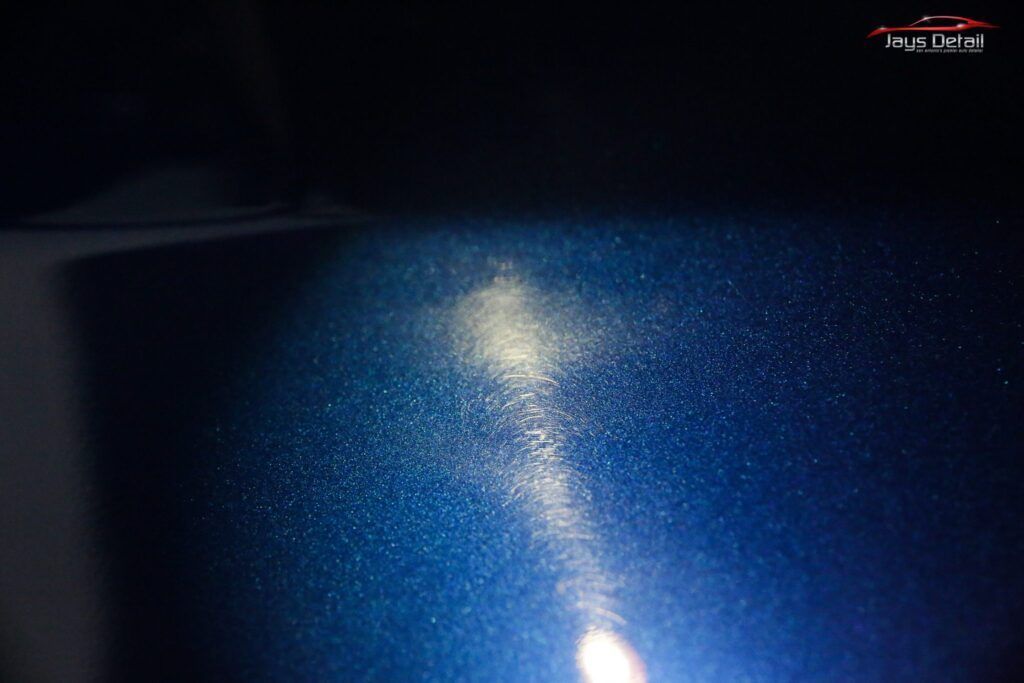 Close-up of a dark blue car surface with a bright streak and scattered white specks, possibly damage or residue.