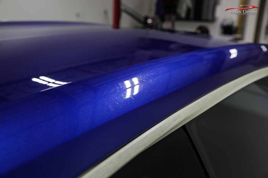 Blue car roof reflecting bright lights in a garage setting.