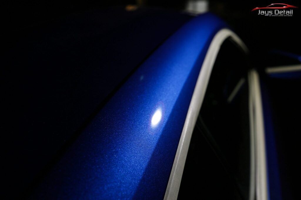 Close-up of a blue car's glossy surface with white trim and a bright highlight.