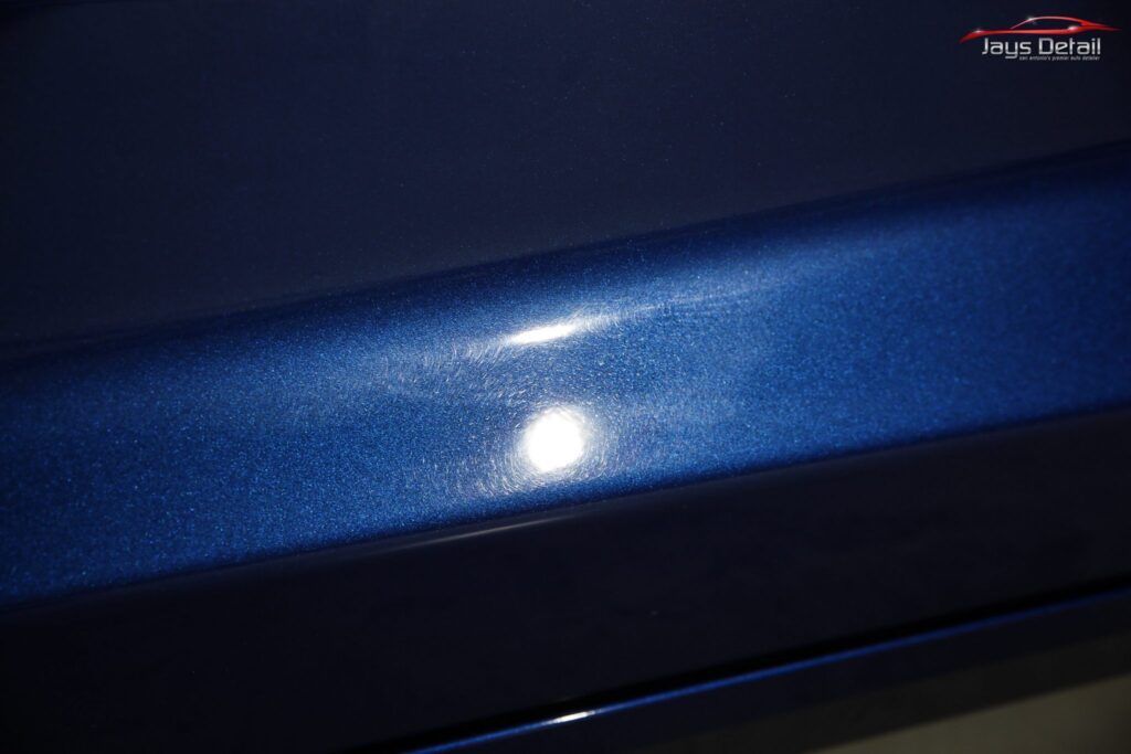 Close-up of a dark blue car surface reflecting light, showing paint imperfections.