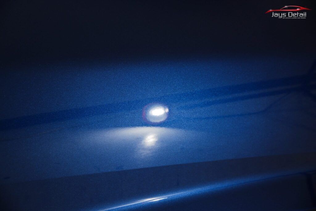 Close-up of a blue car's paint with a single, bright light reflecting off the surface.