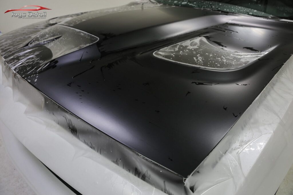 Black car hood with air vent, wrapped in protective plastic.