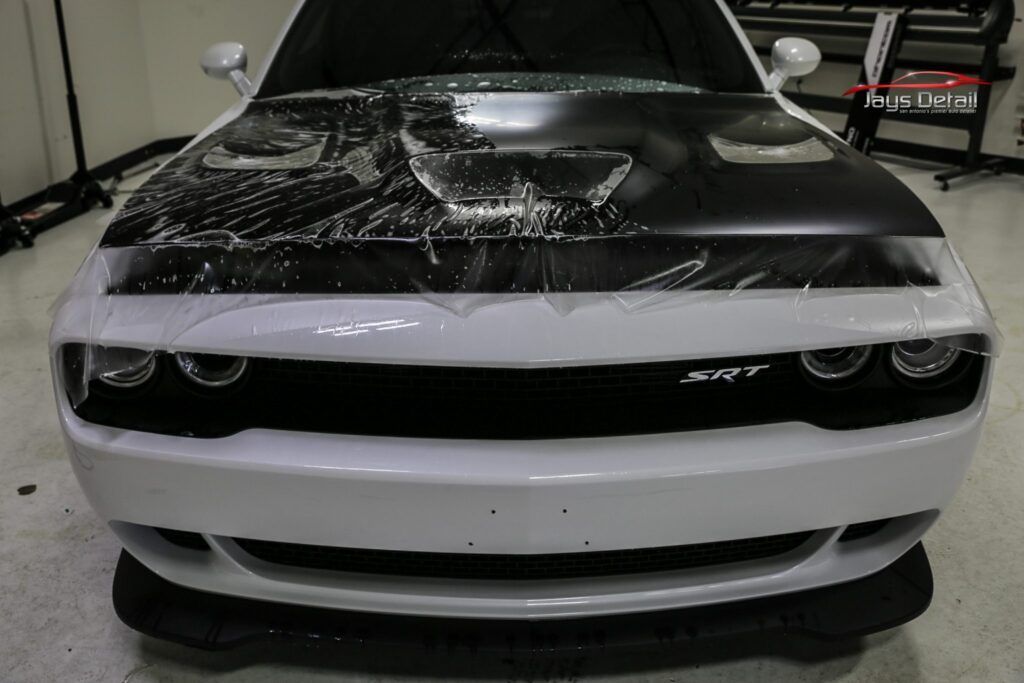White Dodge Challenger with partial clear wrap on hood, in a workshop.