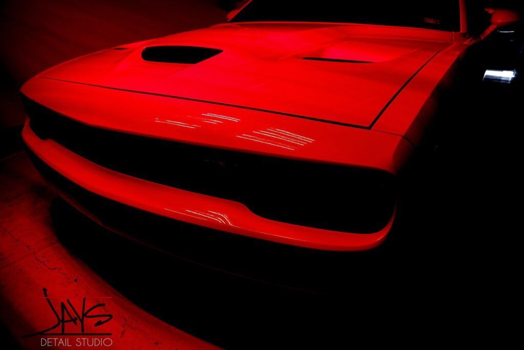 Red-lit Dodge Challenger's front end, angled shot; dark setting.