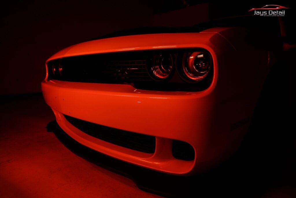 White Dodge Challenger front end illuminated by red light.