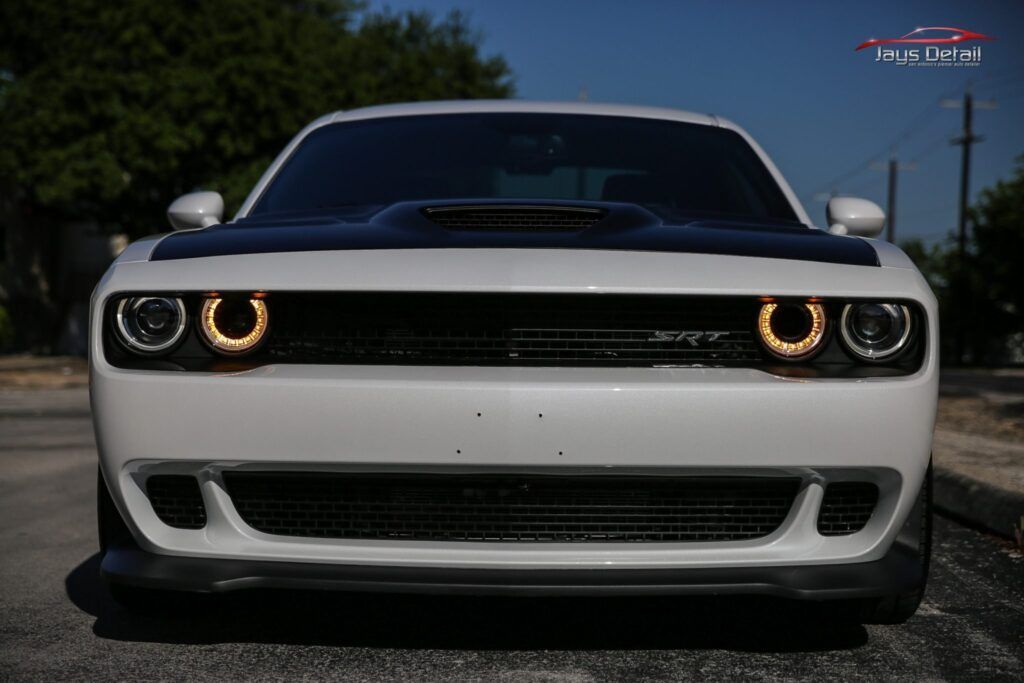 White Dodge Challenger with black hood, glowing orange halo headlights.