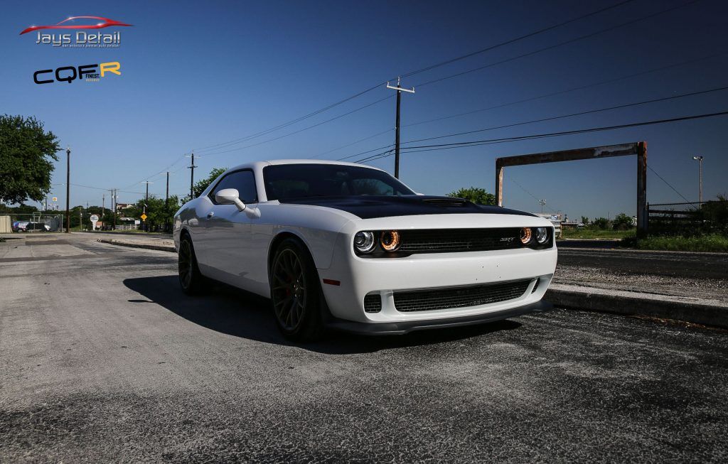 White Dodge Challenger with black hood parked on a paved road, sunny day.