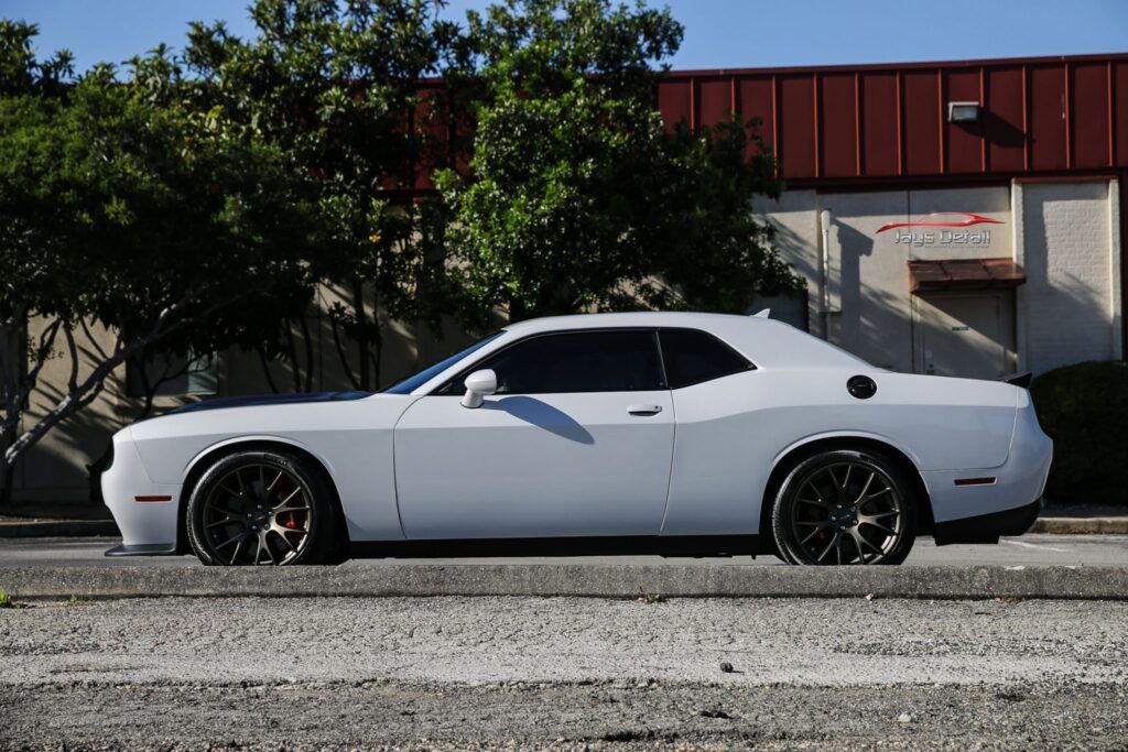 White Dodge Challenger parked on a street with tinted windows and dark rims in front of a building.