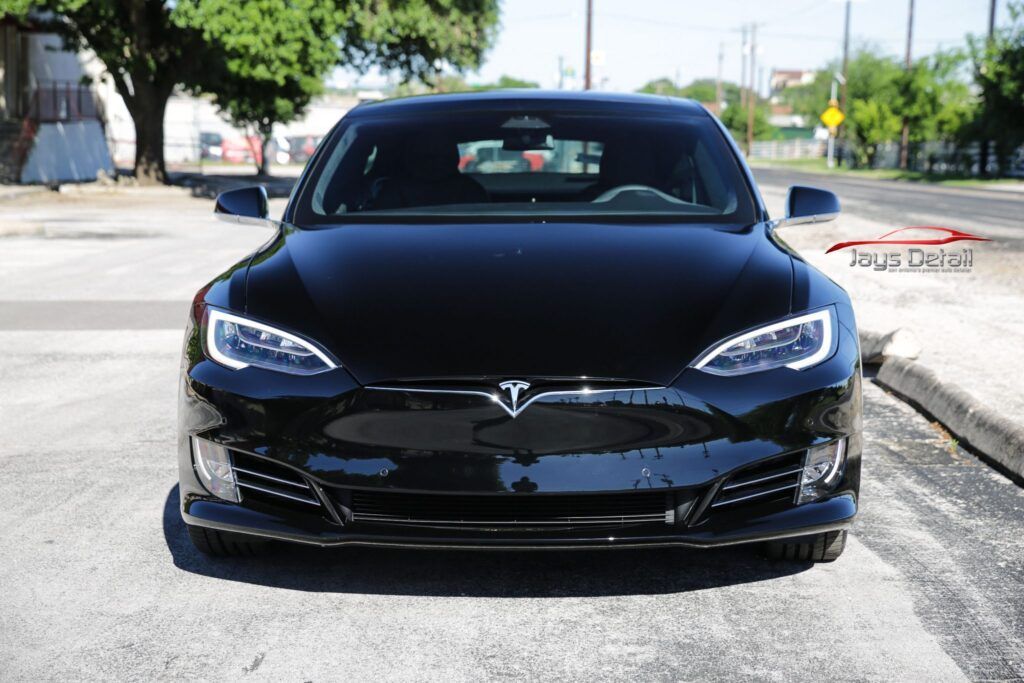 Black Tesla sedan parked on a street, facing the camera, with bright headlights.