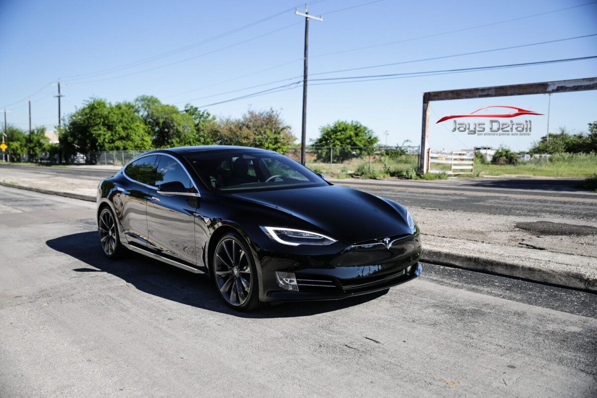 Black Tesla car parked on a street on a sunny day, with a business sign in the background.