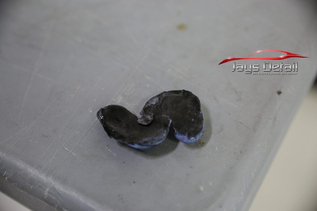 Dark, curved piece of rubber on a gray surface. Appears worn and damaged.