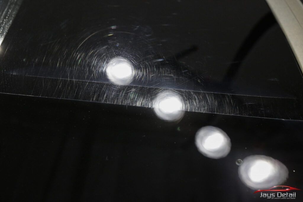 Black car paint with swirl marks, reflecting bright lights.