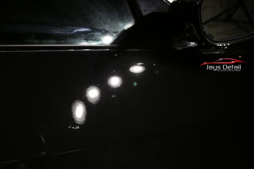 Black car door reflecting bright lights.