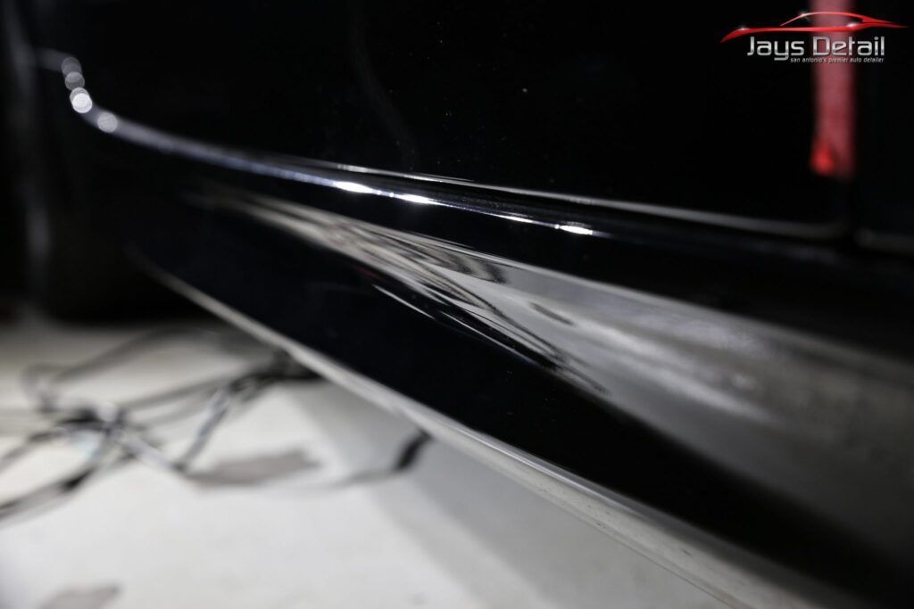 Black car's side skirt with reflective shine, showing imperfections and detailing work.