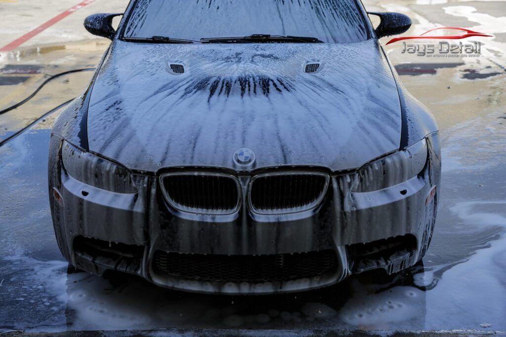 Gray BMW car covered in white foam, being washed.