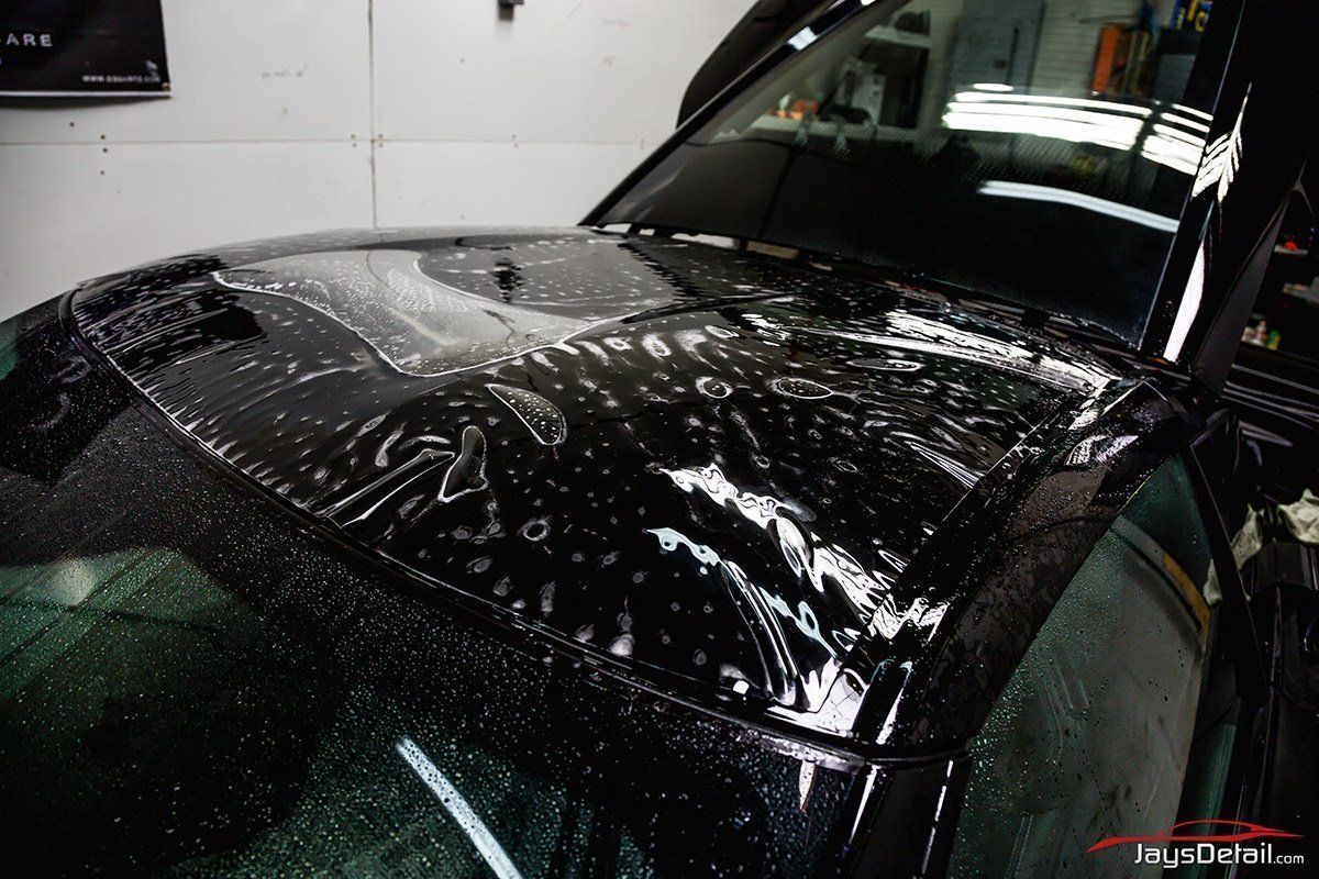 Clear protective film being applied to a black car's hood.