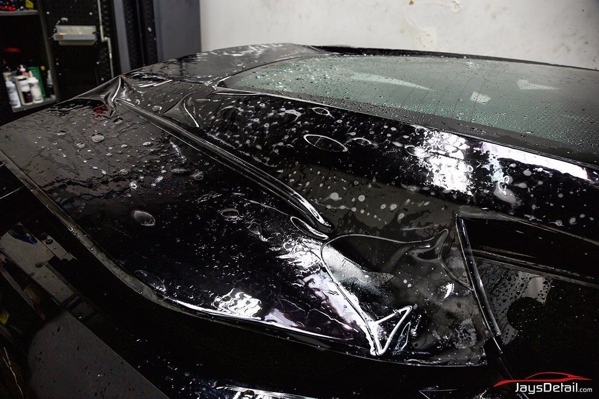 Black car hood covered in wet clear film, possibly for paint protection.