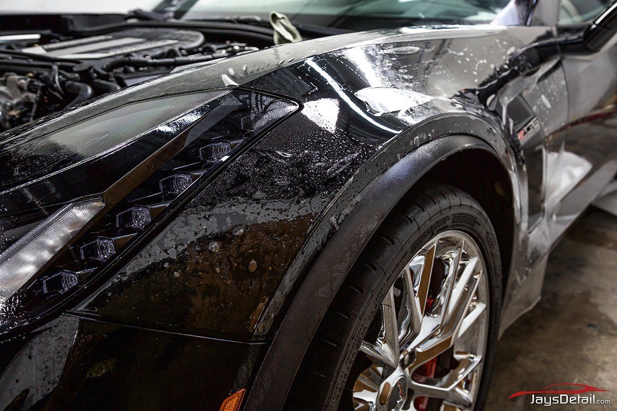 Black car fender with water droplets and chrome wheel.