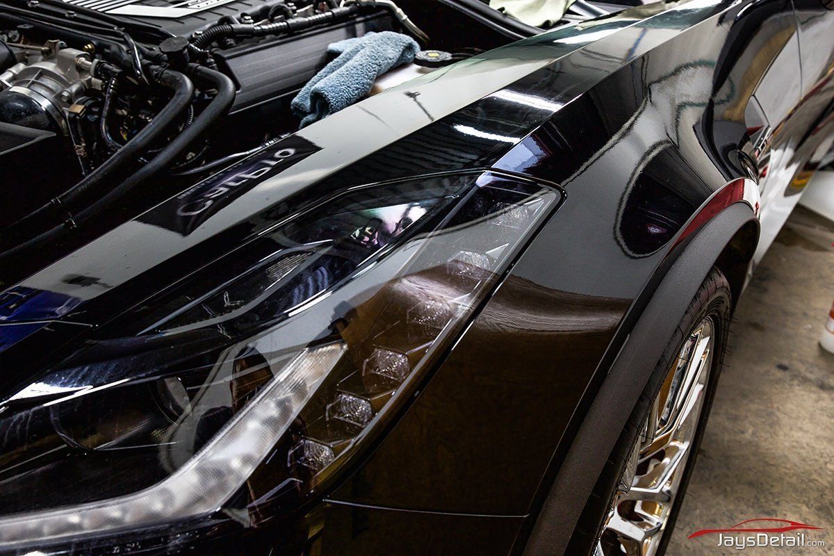 Shiny black car headlight and hood, reflecting surrounding garage.