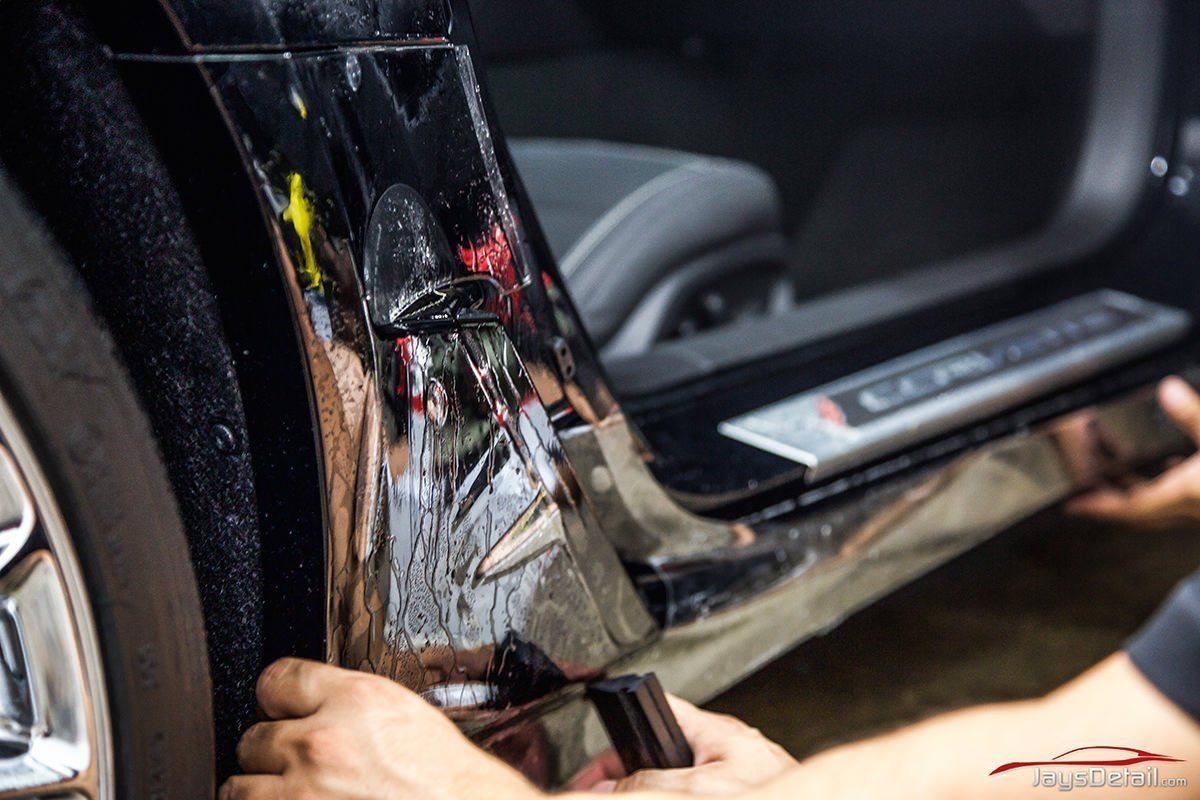 Applying protective film to a car door sill; black car, hands working, close-up.