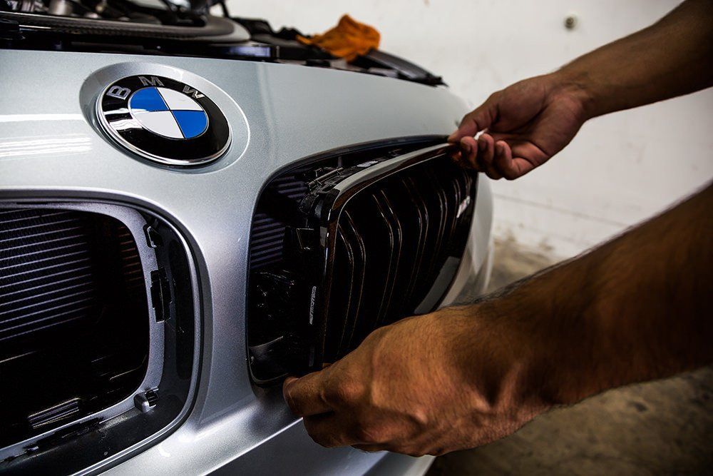 Person installing a black car grill on a silver BMW.
