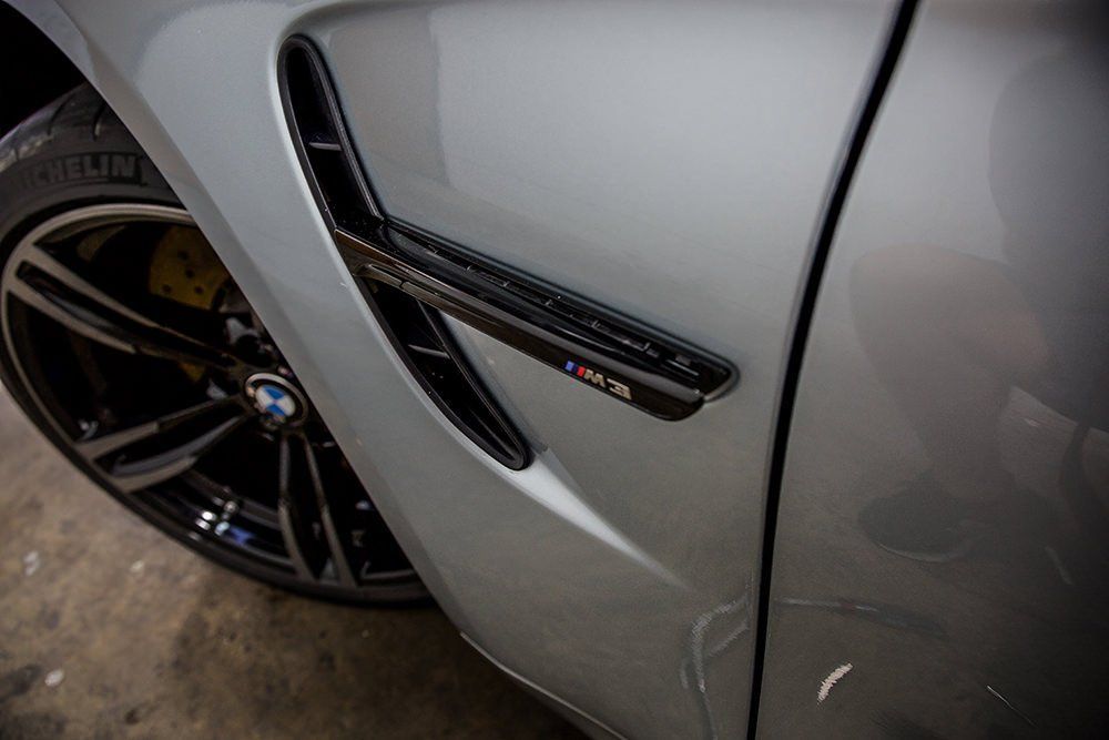 Close-up of silver BMW car side, showing black wheel, vent detail with