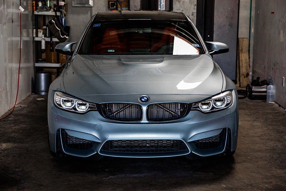 Gray BMW M4 parked in a garage. Black grille, black roof, red interior, silver side mirrors.