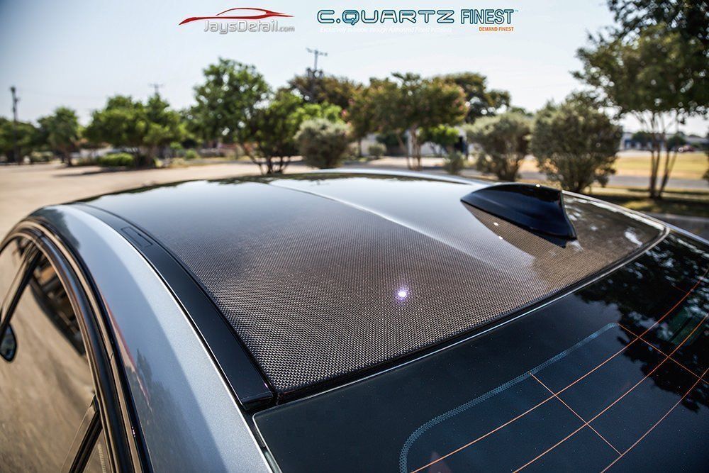 Carbon fiber car roof, glossy finish, with shark fin antenna, outdoors.