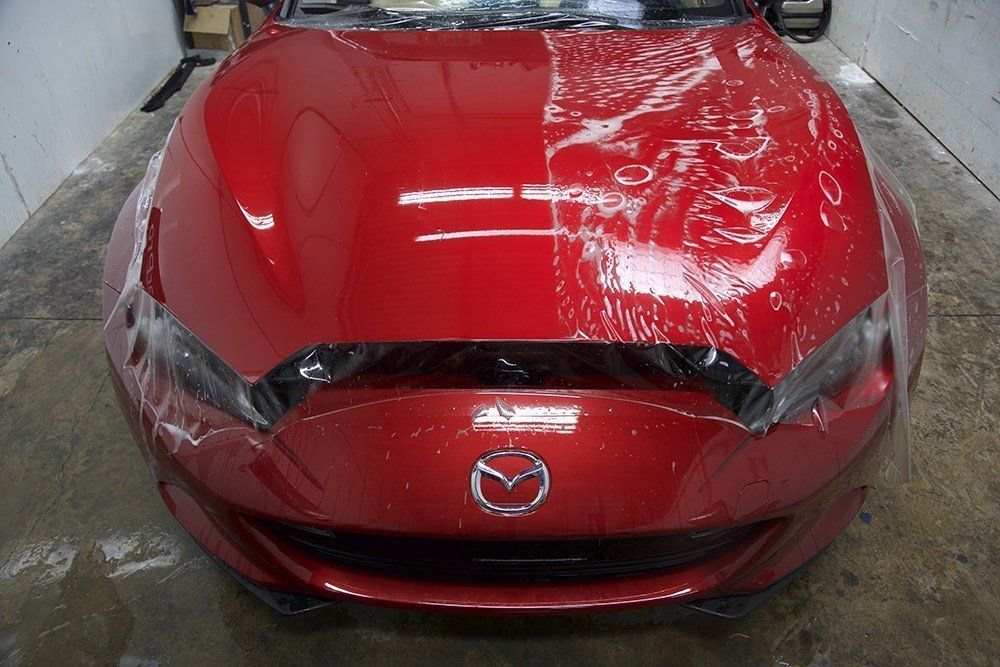 Red Mazda car hood partially covered with protective film.