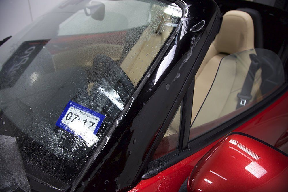 Red sports car interior; windshield, driver's side view. Texas license plate visible. Beige seats, black trim.