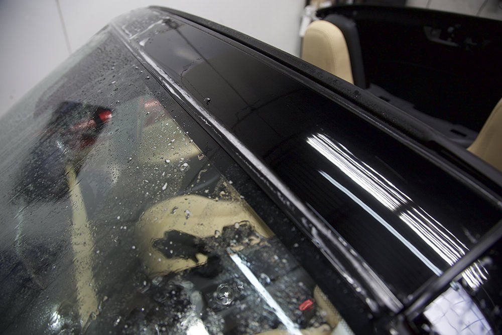 Close-up of a car's windshield with water droplets, focusing on the upper corner and black frame.