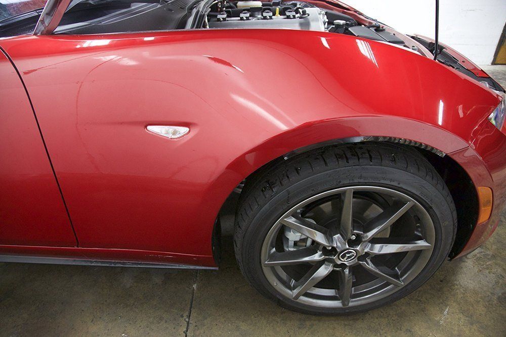 Red car with a damaged front fender and wheel, indoors.
