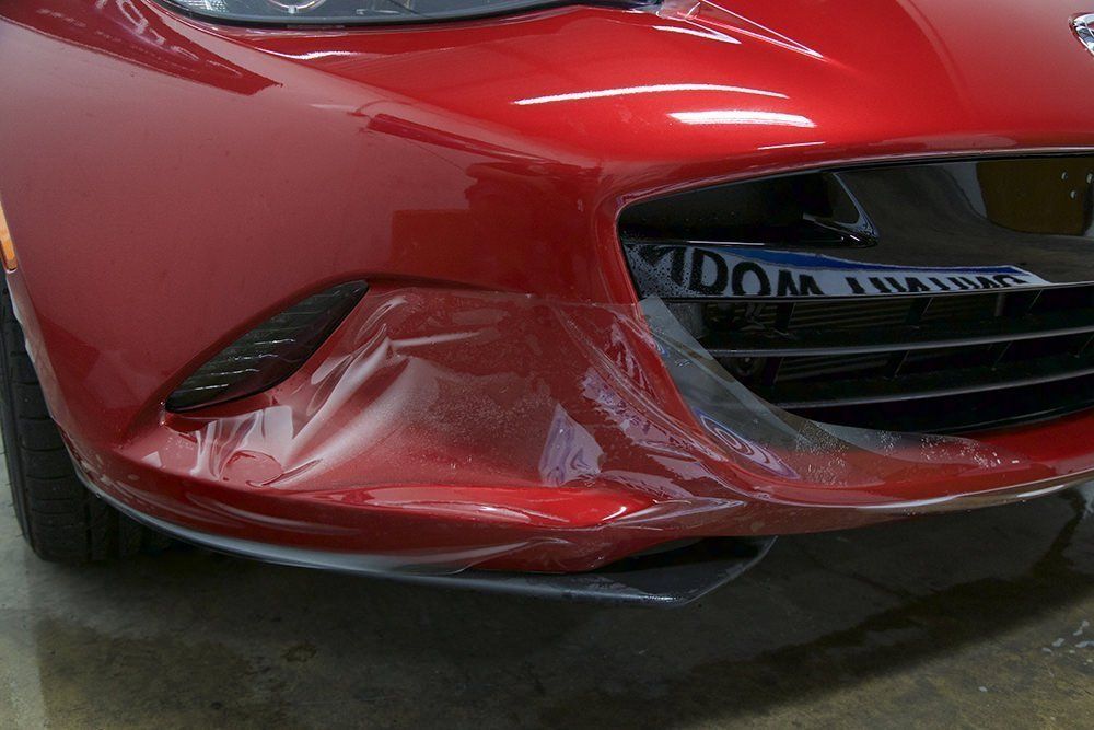 Red car bumper with clear protective film peeling off.