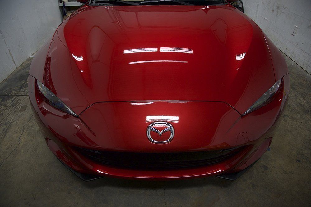 Red Mazda car front view, headlights and logo visible, in a garage.