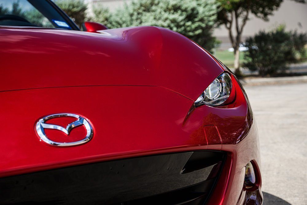 Red Mazda Miata car, front view, chrome logo, glossy paint, parked outdoors.