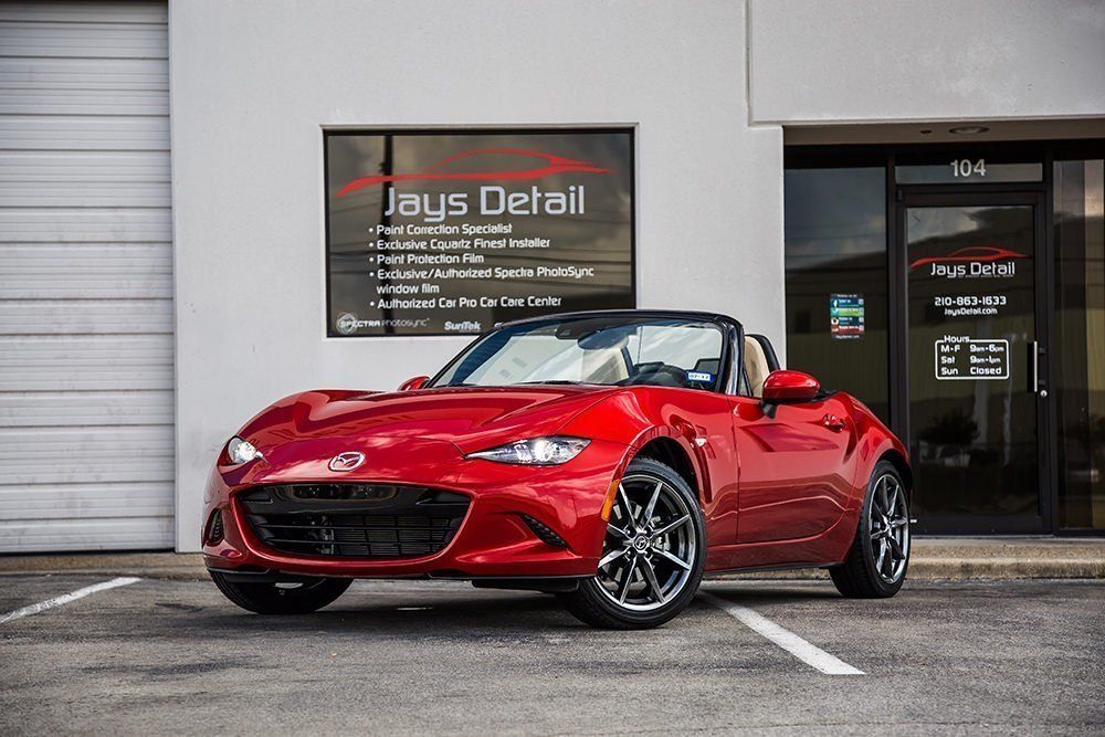 Red Mazda Miata convertible parked outside a detailing shop.